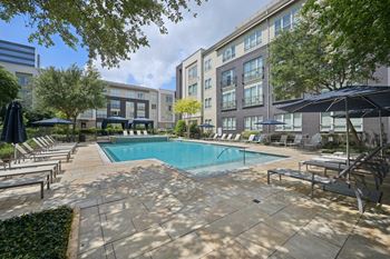 A swimming pool surrounded by lounge chairs and umbrellas in a courtyard.